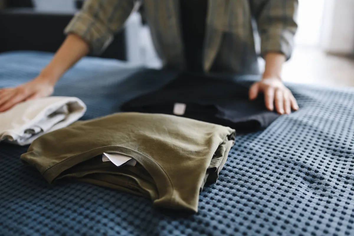 Hands sorting folded clothes on a bed